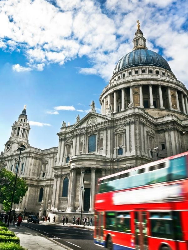 a red double decker bus passing a cathedral in London England