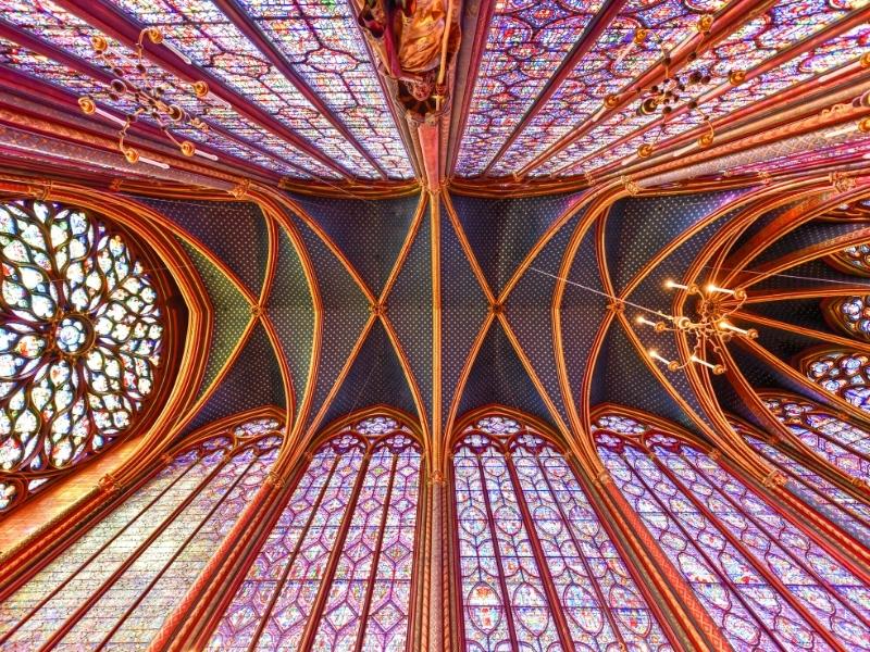 a high wooden roof in a French cathederal surrouned by stained glass windows