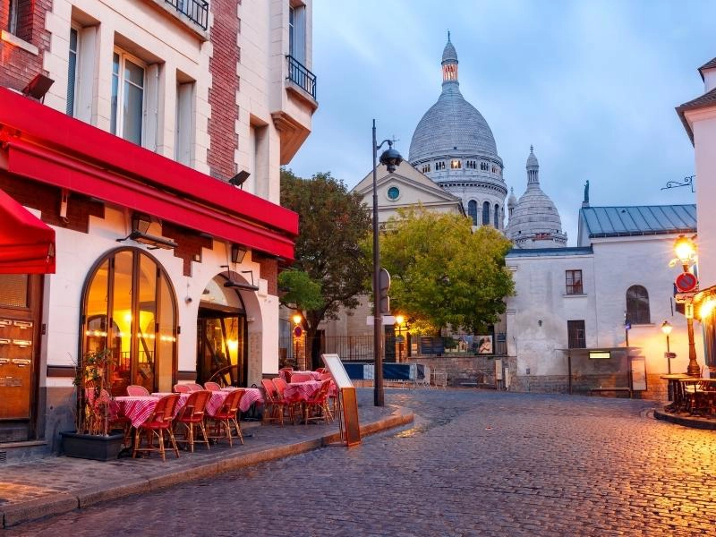 cobbled street with cafes and tables outside, Sacre Couer in the distance