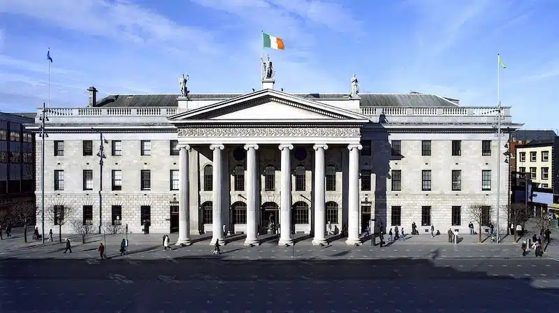 Large pale stone building with a portico and columns at the front. flying the Irish flag