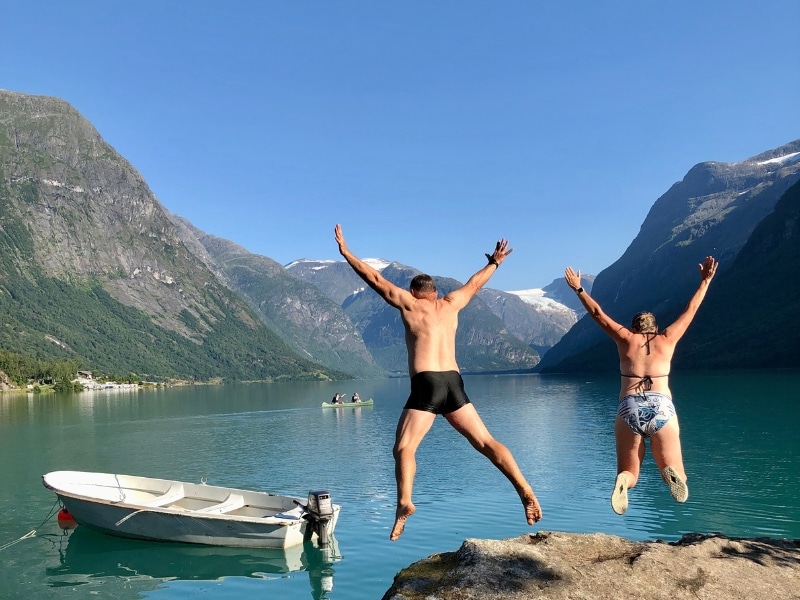 couple jumping from a rock into a glacial lake