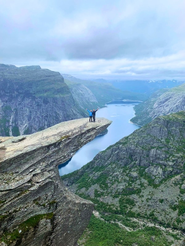 couple tanding on Trolltunga with a fjord in the background