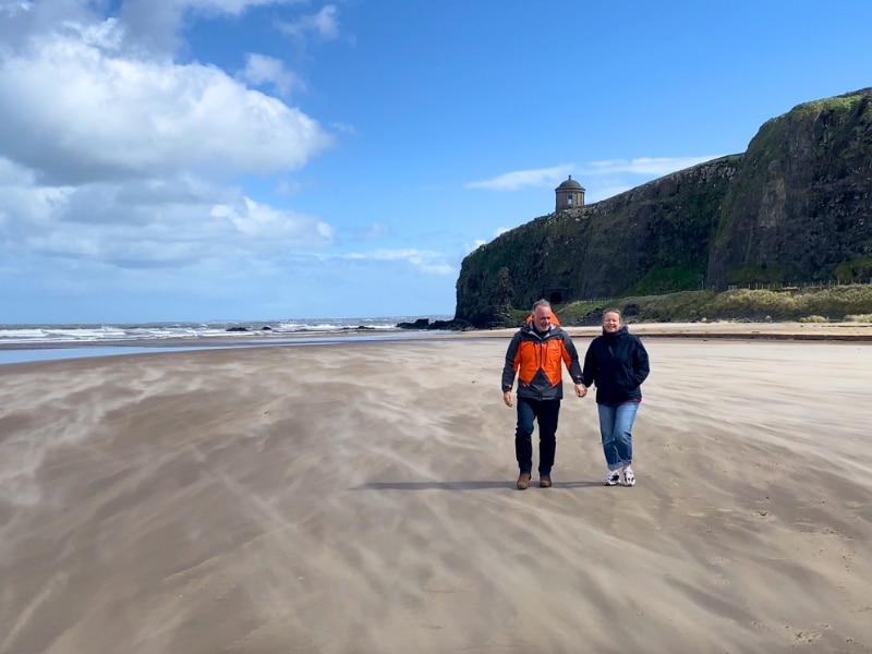 Couple walking on a beach with a clifftop temple in the distance