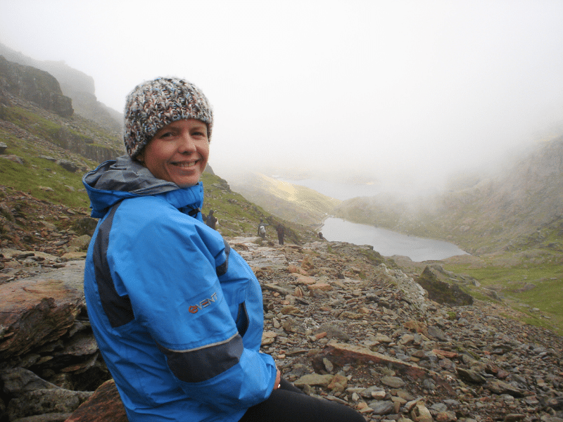 Woman in a blue coat and wooly hat on a cloudy mountainside