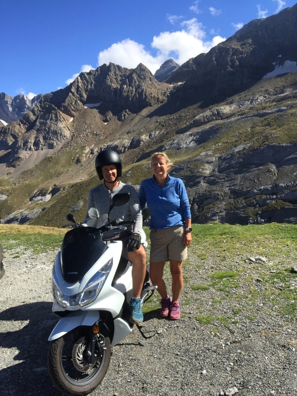 man wearing an open faced helmet on a white scooter with a woman standing next to him