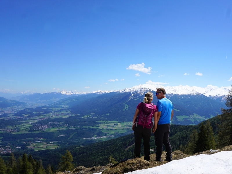 Cuple in hiking gear looking across a deep green valley to snow capped mountains