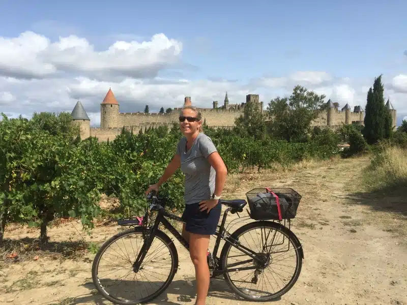 woman on a bike surrouned by trees with a turreted castle in the background