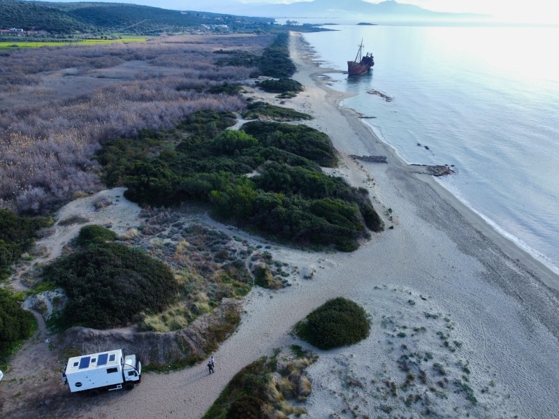 drone footage of overlander parked on a beach with a shipwreck in the distance