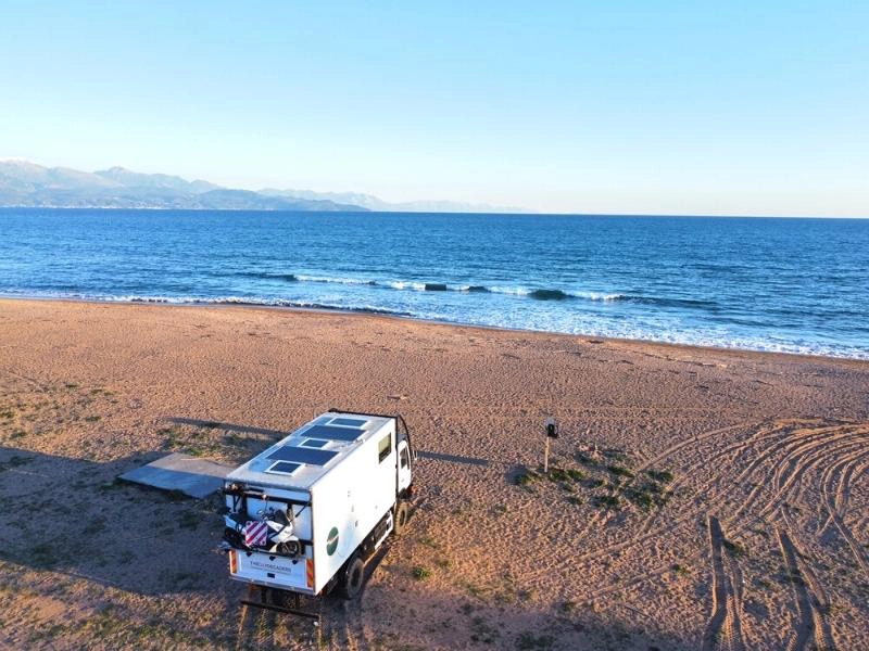 white overland truck parked on a beach with blue sea in the background