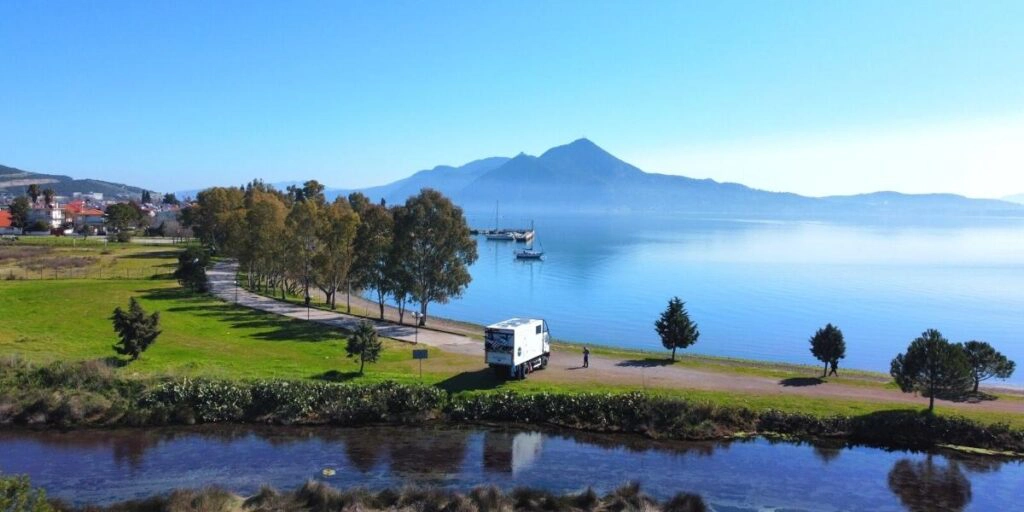 whaite truck parked between a river and the sea in Greece with mountains in the distance