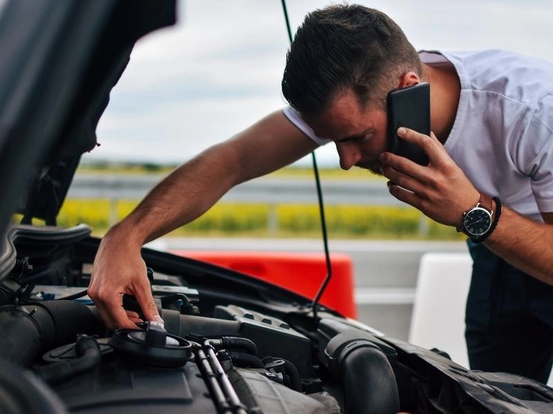 Man looking at a car engine whilst on the phone