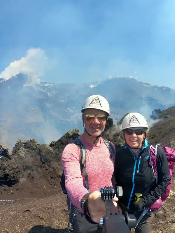 couple taking a selfie wearing hard hats by a live volcano