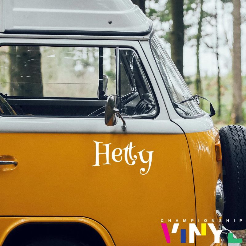 This is an image of the side of a bright orange VW Bus, it has the name Hetty written on the side in a fun font.
