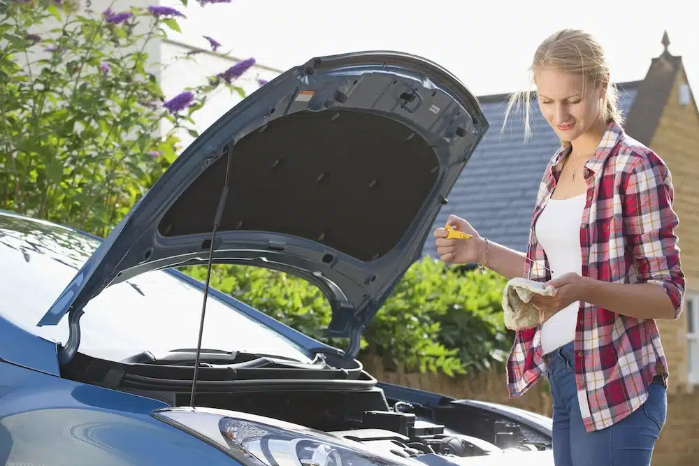 Woman ina. checked shirt checking the oil level in a car