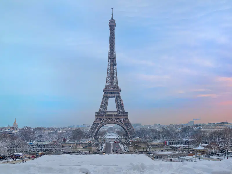 Eiffel tower surrounded by snow against a pink and blue sky
