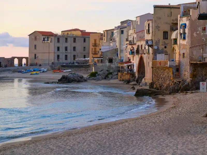 Town beach backed by houses with colorful boats in the distance