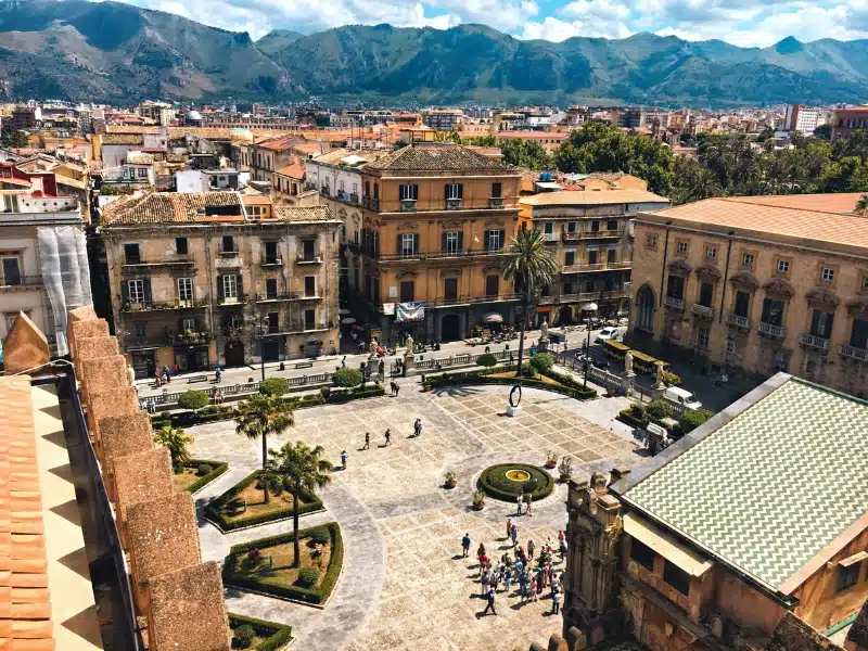 View over historic buildings around a piazza to distant mountains 