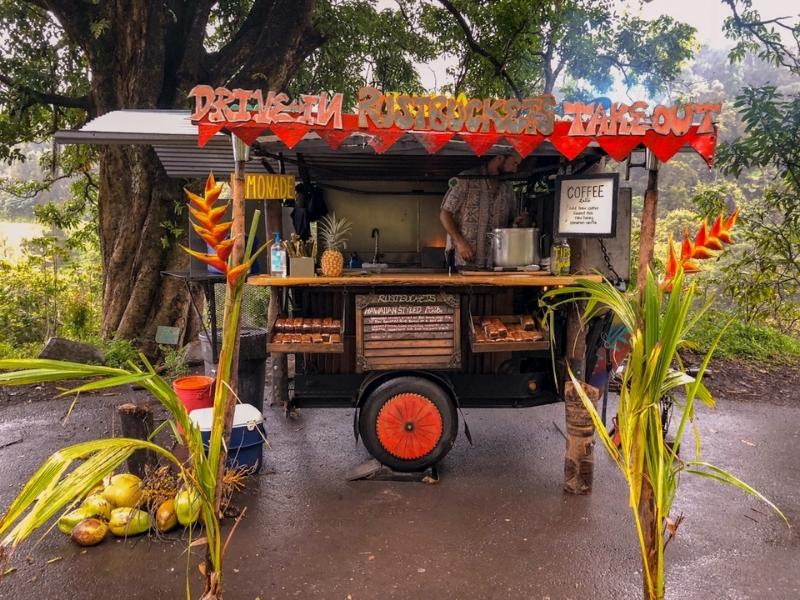 Street food stall with red flags and wheels serving coffee and lemonade with coconuts on the ground and exotic plants 