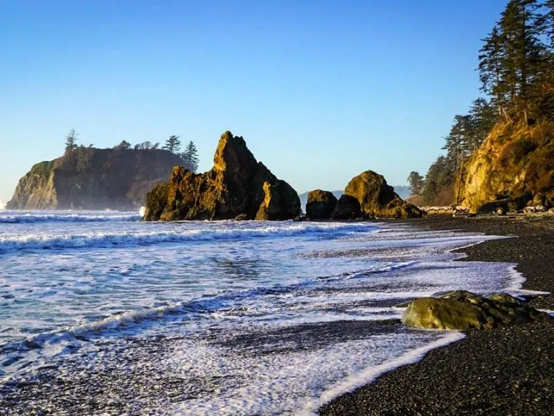 Black shingle beach with rock formations protruding into the water