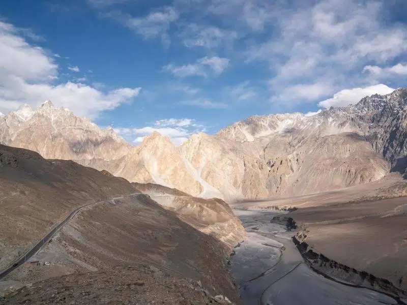 Road along the side of a treeless mountains with a river bed below