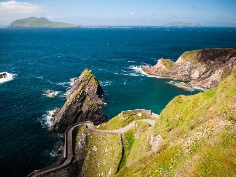 Narrow road surrounded by grass down a cliff towards the Atlantic Ocean in Ireland