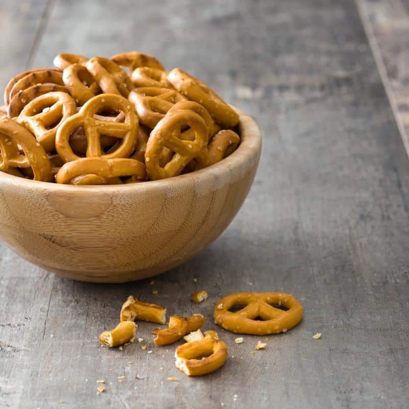 An image of a wooden bowl filled with pretzels, and some pretzels on the table.