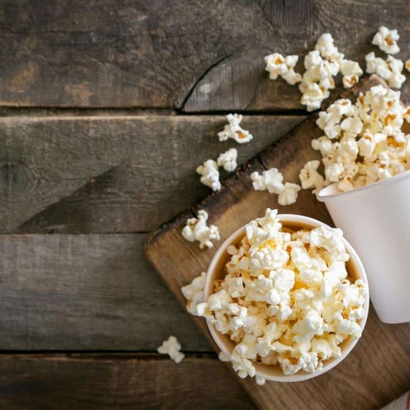 An image of popcorn in a paper cup on a wooden table.