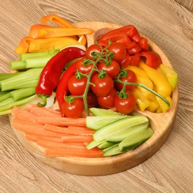 A wooden platter filled with vegetable sticks and cherry tomatoes.