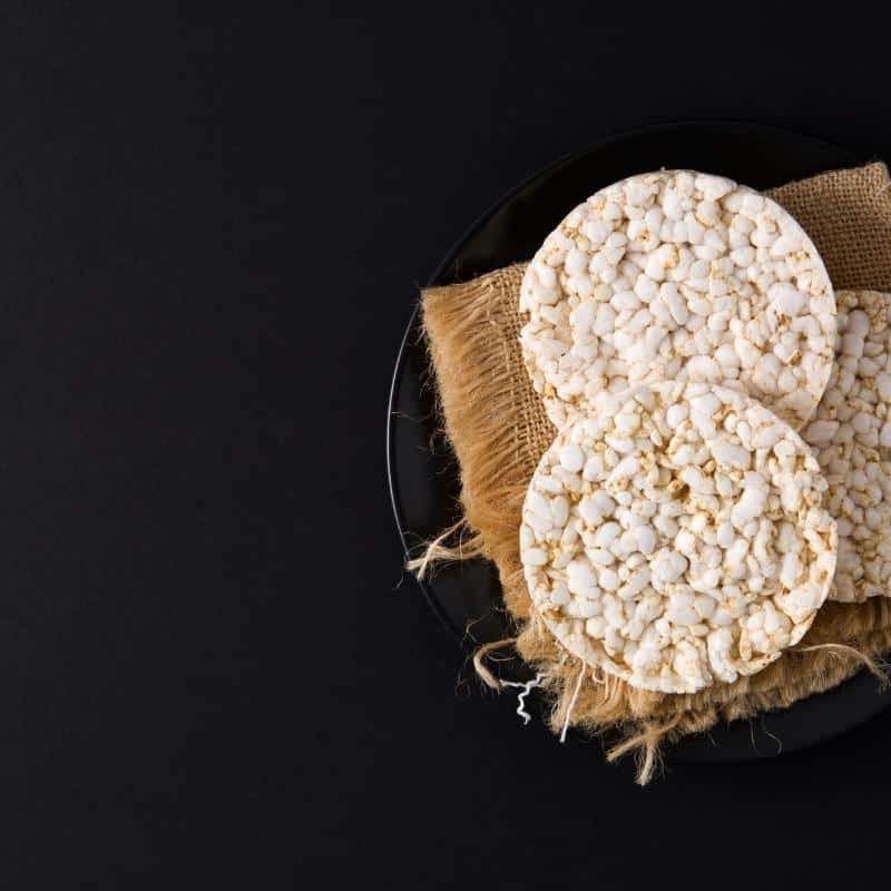 A black background with a a black plate and hessian cloth with two rice cakes on top.
