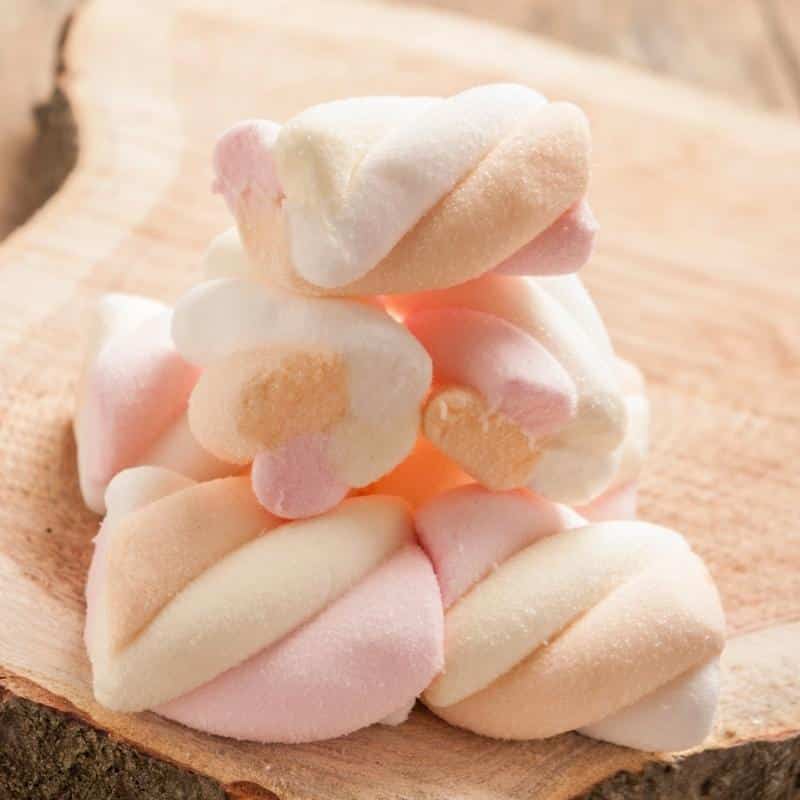 An image of twisted yellow and pink marshmallows on a wooden table.