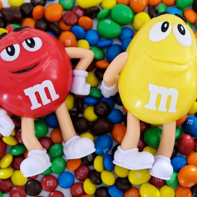 A photo of multi coloured M&M's with two large M&M with faces, arms and legs.