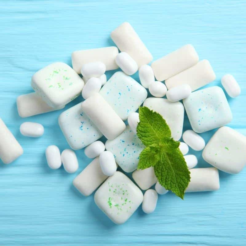 A blue background with a selection of mint sweets and a small sprig of fresh mint.