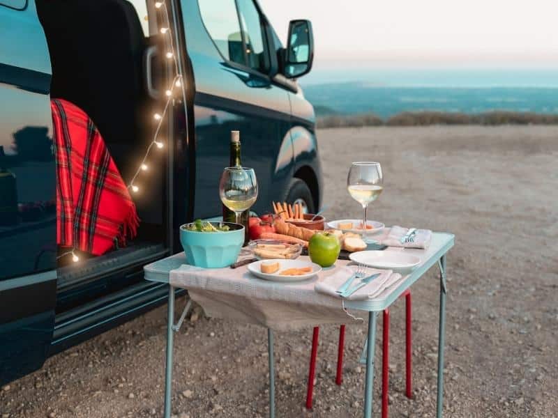 A campervan parked on the beach with a fold-up table set up. On the table is a picnic and two glases of wine.