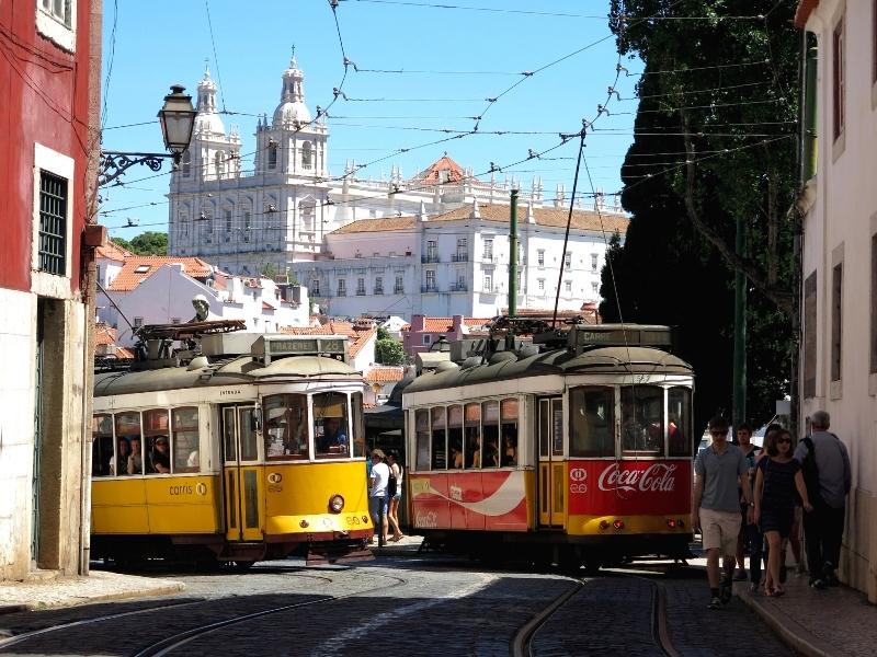 Red and yellow trams rounding a corner in Lisbon with the  Monastery of São Vicente de Fora in the background.