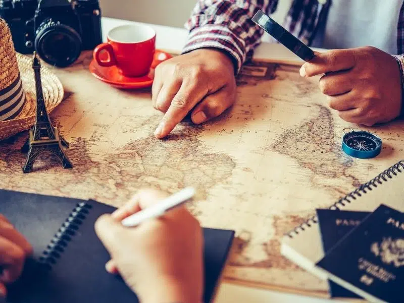 People using a map, compass and magnifying glass to plan a trip.