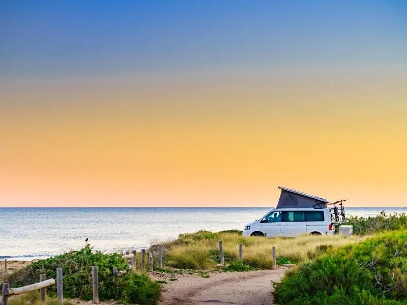 VW campervan with a pop top roof parked amongst grasses and bushes overlooking the sea.