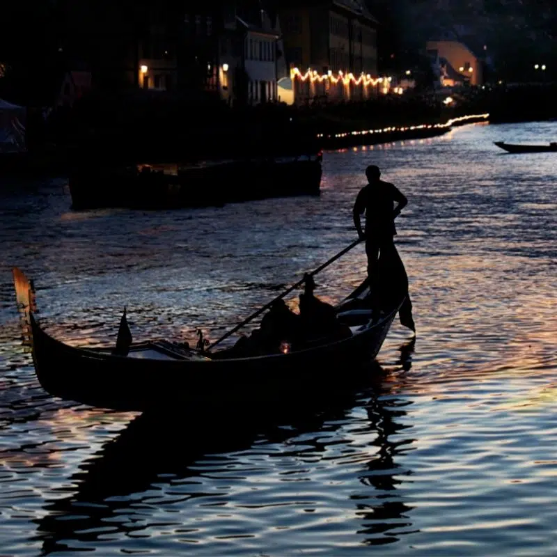 An image of a gondola at night, with building lights in the background