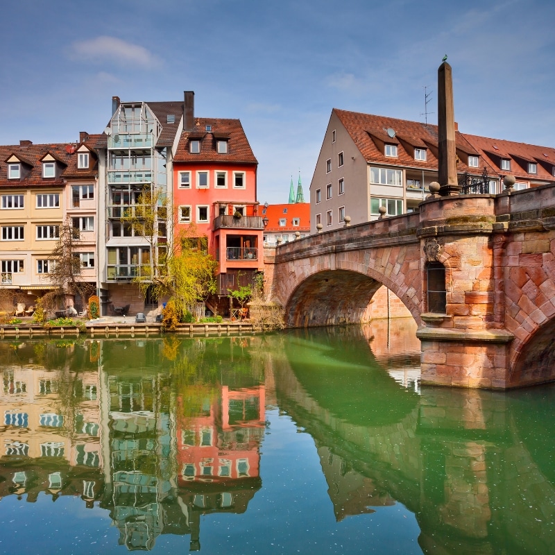 A photo of Nuremberg, with a river and old bridge on the forefront.