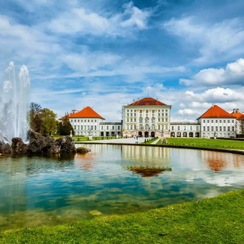 An image of Nymphenburg Palace, with a lake and fountain in the forefront.