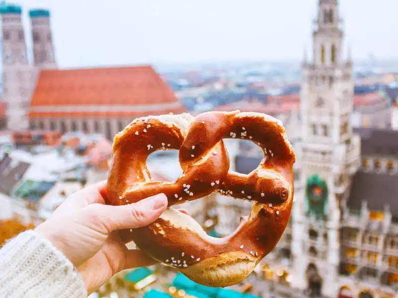 Hand with pretzel on the background of the panorama of Munich square, town hall, Christmas fair. Germany in winter.