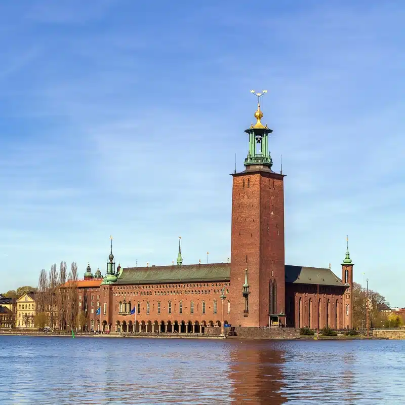 An image of Stockholm City Hall, built out of red brick with a tower, on the water.