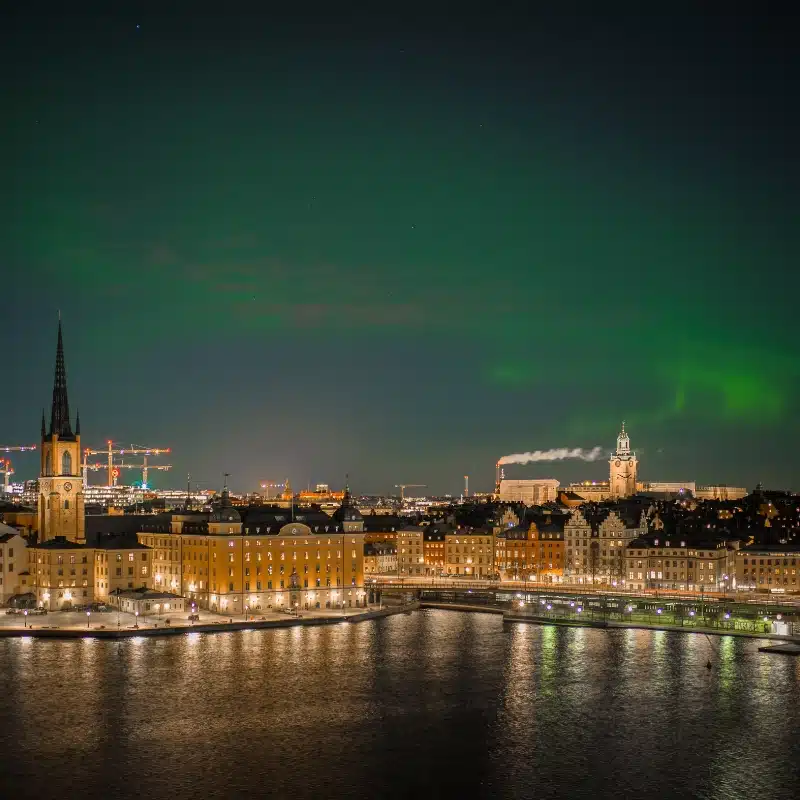 An image of Stockholm at night taken across the water.  The northern lights are in the sky