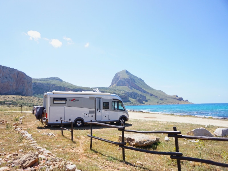 A class motorhome parked facing a beach and the sea with mountains behind