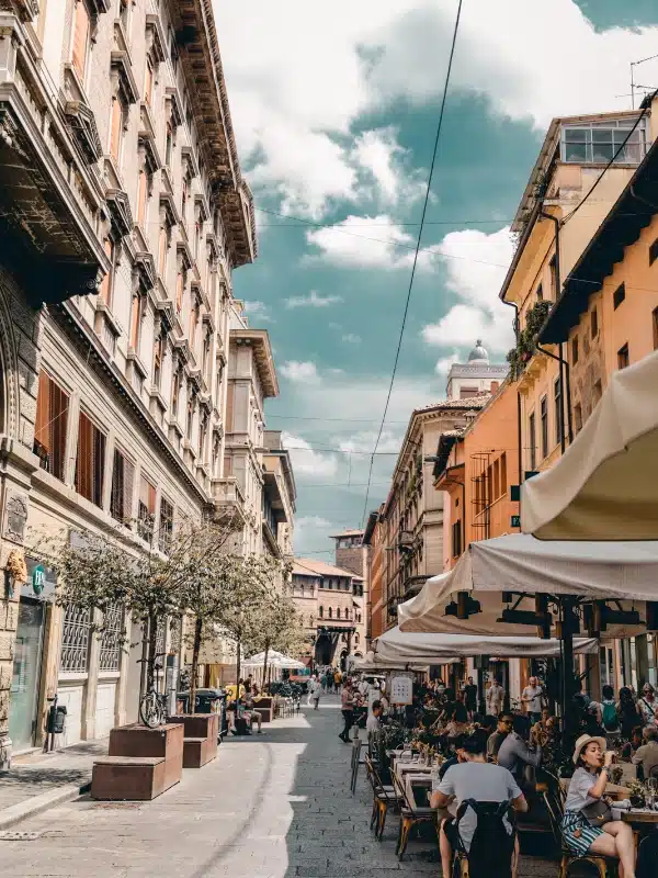 diners eating al fresco under sun shades on a leafy street lined with historic buildings