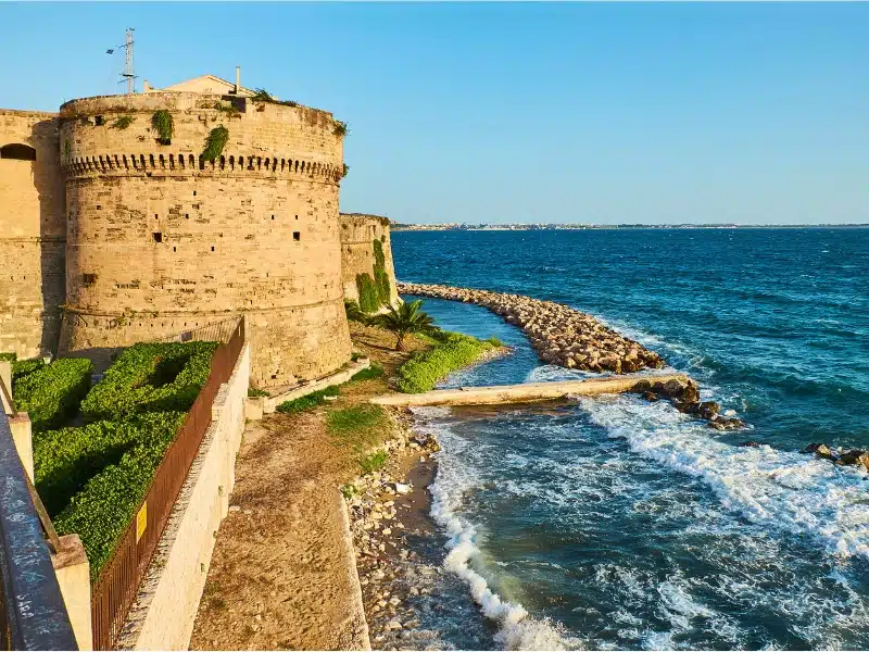 a creamy coloured round castle next to the sea