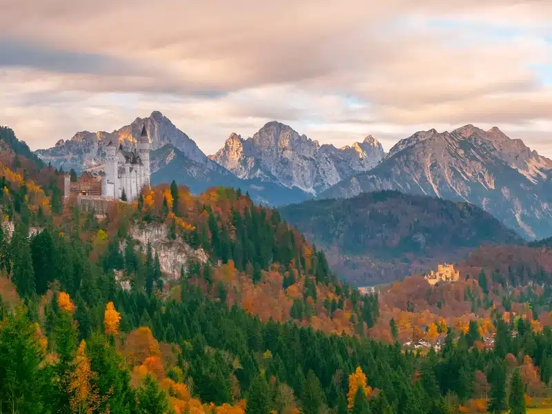 mountains with one white castle in the foreground, and another castle in the distance