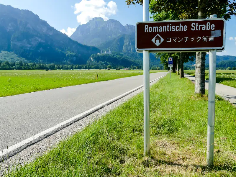 romantic road sign on a grassy verge with a white castle in the distance