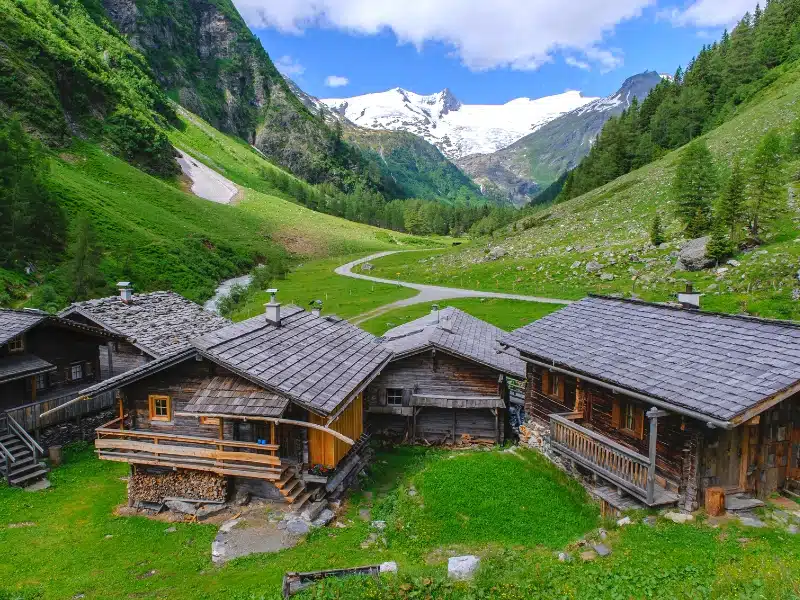 snow capped mountains with wooden huts and green pastures in the foreground