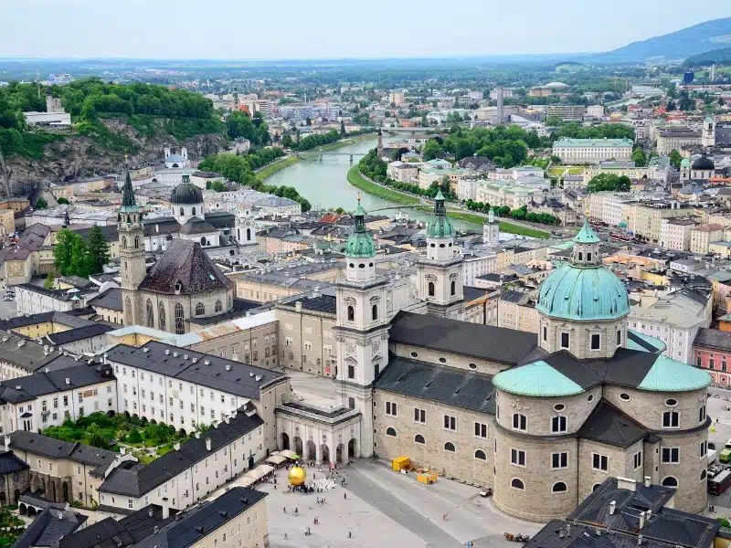 An Austrian city on a river with a large palace in the foreground with verdis gris domed roofs