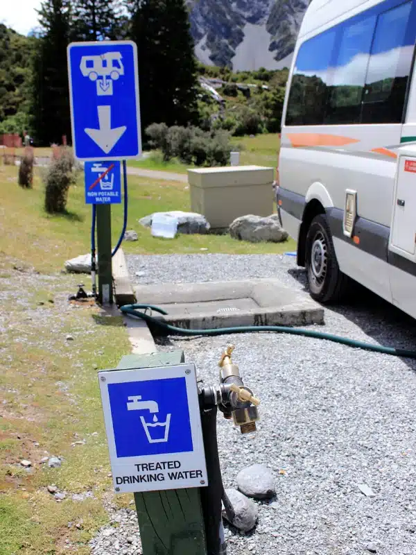 campervan with waste pipe connected going into sewer. Blue signs show treated drinking water and non potable water.